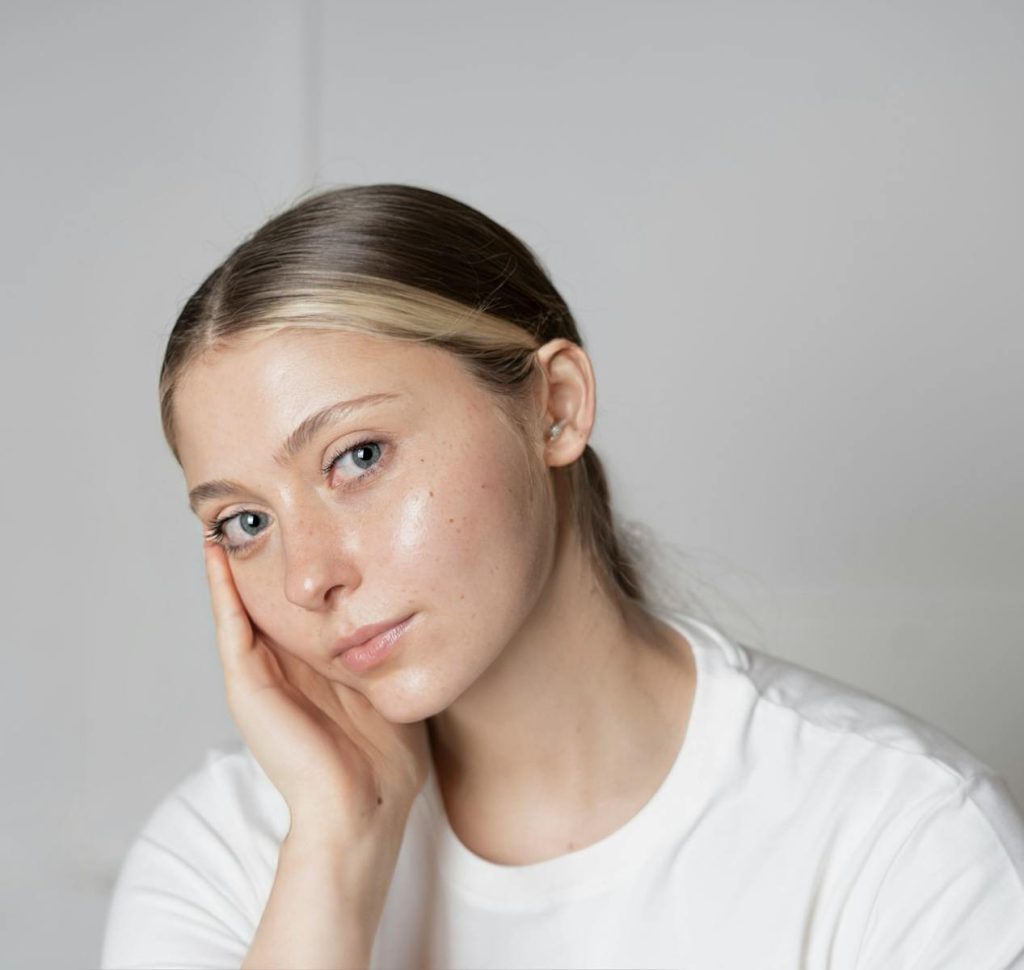 Close-up portrait of a young woman with clear skin and a thoughtful expression indoors.