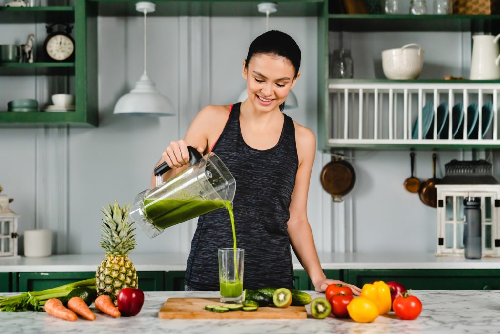 Healthy young woman drinking fresh detox juice in the kitchen