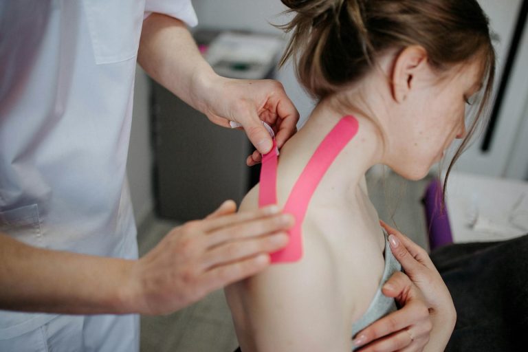 A physiotherapist applies kinesio tape to a woman's shoulder for pain relief and treatment.
