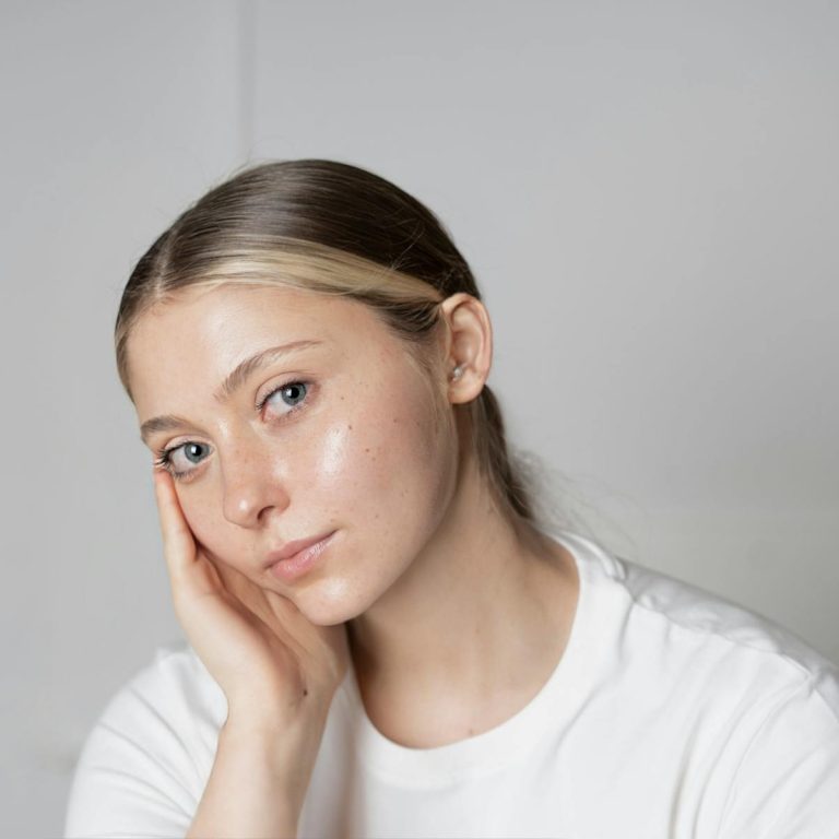 Close-up portrait of a young woman with clear skin and a thoughtful expression indoors.